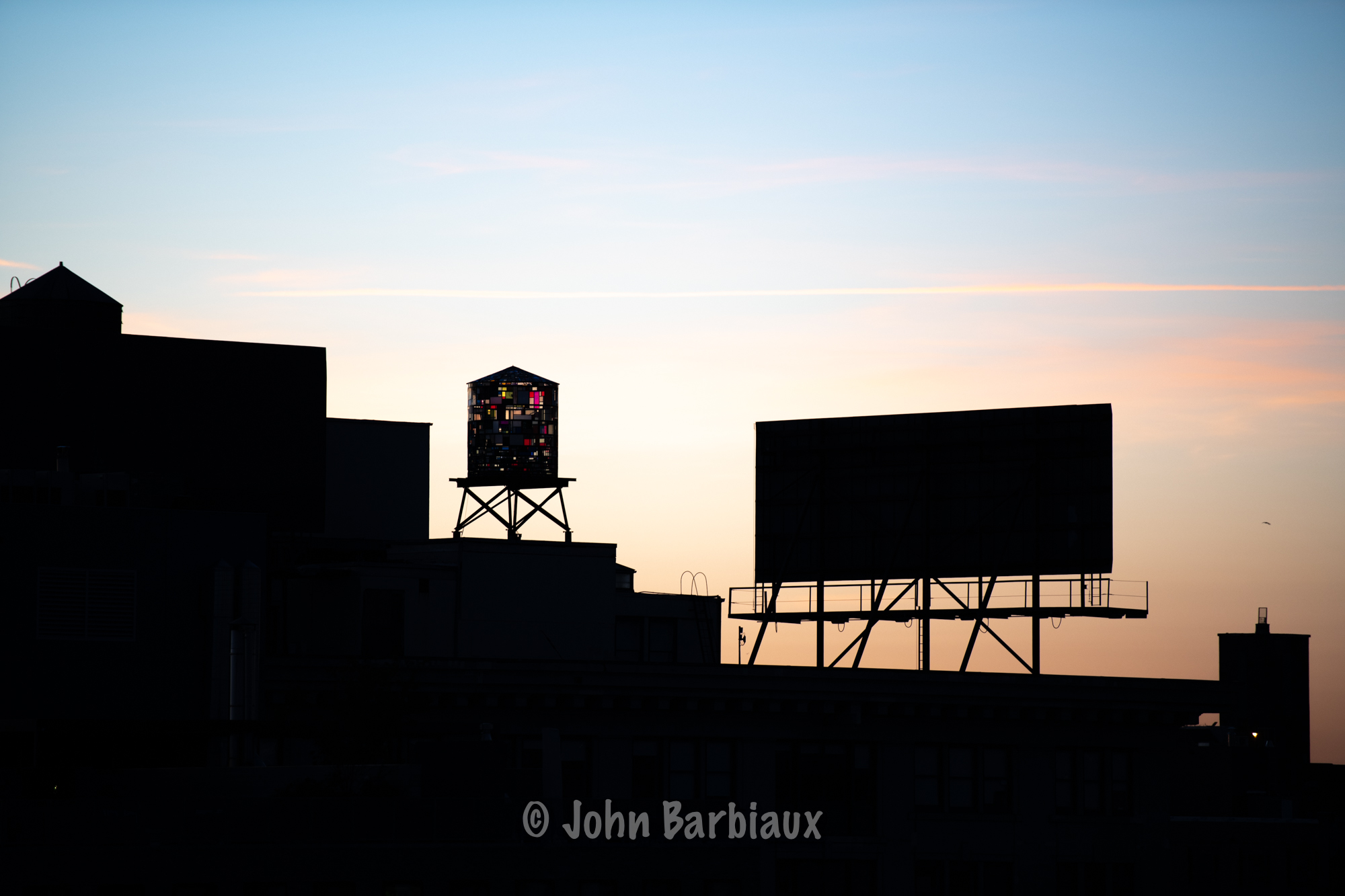 A silhouette of a colorful water tower built by artist Tom Fruin in Brooklyn New York at sunrise.